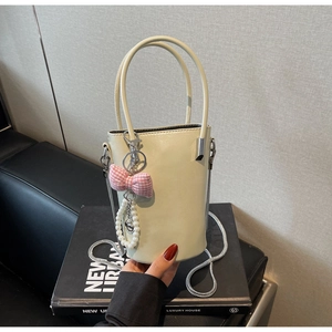 Detail der cremefarbenen Beuteltasche mit Metallkette, Schleife und Perlenanhänger