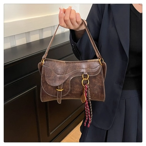 Detail of dark brown vintage saddle bag featuring metallic buckle and woven tassel charm