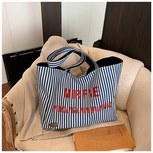 Close-up of blue striped canvas tote bag featuring red lettering and handmade leather patch
