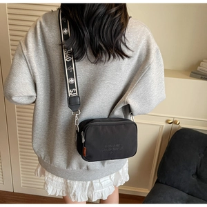 Detail of black nylon camera bag with embroidered text and wide jacquard strap