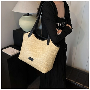 Detail of woven straw tote bag with black leather shoulder straps on a female model