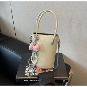 Detail einer cremeweißen Beuteltasche mit rosa Schleife und Perlenanhänger Verzierung