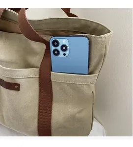 Detail showing the durable canvas tote outer pocket with a leather patch and smartphone