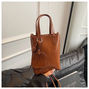 Detail of a brown leather bucket bag with dog charm and embossed logo on black leather background