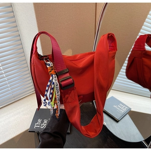 Detail of red crescent crossbody bag with woven 'NICENICE' charm and wide strap