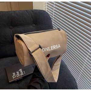 Detail of khaki cylindrical canvas bag with wide strap on sofa in soft lighting