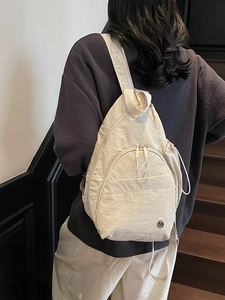 Minimalist beige nylon backpack with textured finish shown on a model in a stairwell