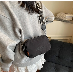 Detail of black canvas crossbody camera bag with wide woven strap and embossed text