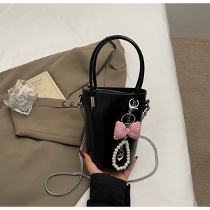 Detail einer schwarzen glänzenden Beuteltasche mit rosa Schleife und Perlenanhänger