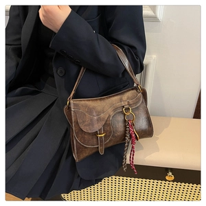 Detailed close-up of brown vintage saddle bag with woven tassel and gold hardware