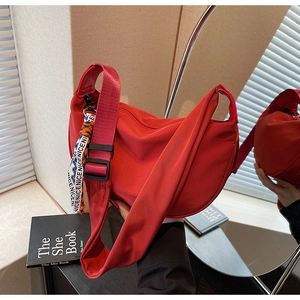 Detail of red nylon crescent bag with adjustable strap and decorative slogan ribbon