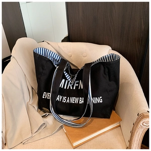 Close-up of black canvas tote bag with white lettering on a beige cozy armchair
