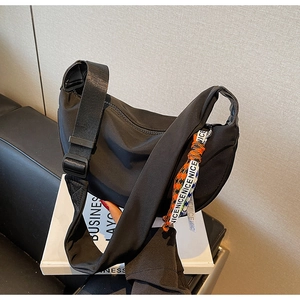 Detail of black nylon crescent bag with adjustable wide strap and a NICE letter charm