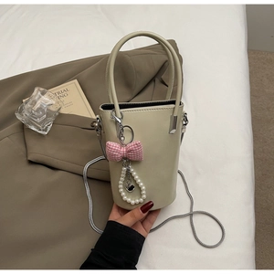 Detail der cremefarbenen Beuteltasche mit rosa Schleife, Perlenanhänger und Silberkette