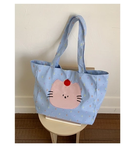 Détail du sac cabas à carreaux bleus et blancs avec broderie chat rose sur un tabouret