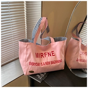 Detail of pink canvas tote with red lettering and blue striped handles on mirror
