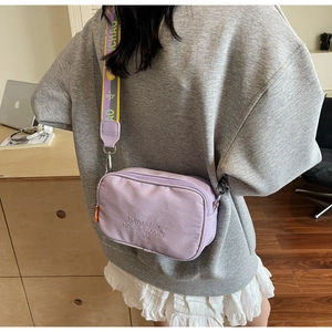 Detail of light purple canvas camera bag with wide patterned strap and slogan embroidery