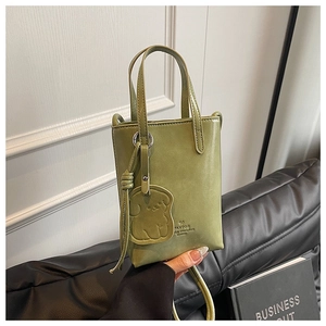 Detail of light green bucket bag with cute dog charm and dual top handles on black cushion
