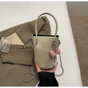 Detail der cremefarbenen Beuteltasche mit rosa Karoschleife, Perle und Kettengurt