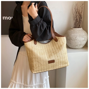 Detail view of woven straw tote bag featuring brown leather handles and brand logo