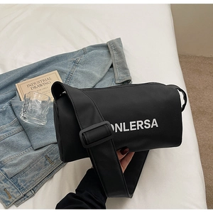 Detail of minimalist black cylinder crossbody bag with wide strap on modern bedding