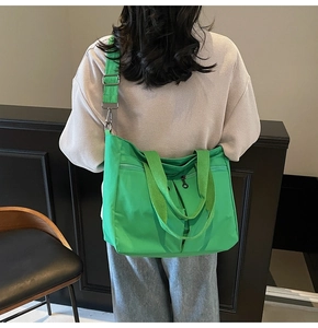 Detail of green nylon tote bag featuring front zipper pocket and wide adjustable strap