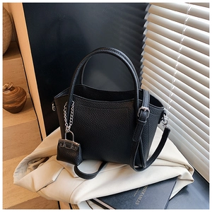 Detail of black lychee grain leather handbag with silver chain lock charm and strap