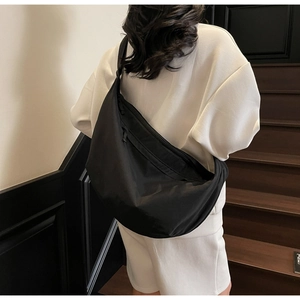 Detail of a large black nylon crossbody bag with wide shoulder strap shown on a model