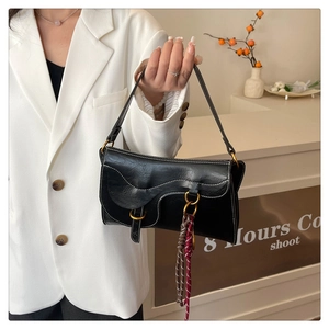 Detail of black saddle bag with vintage gold ring and colorful woven lanyard accessory