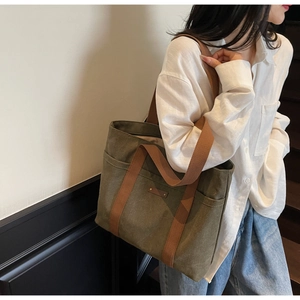 Détail du sac fourre-tout en toile olive foncé avec poignées brunes et poches frontales