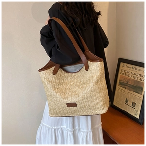 Close-up of a large woven tote bag with brown leather straps and natural straw texture
