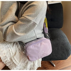 Detail of purple nylon camera bag with embroidered text and colorful striped strap