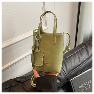 Detail of mini sage green bucket bag with dog charm and embossed logo on leather surface