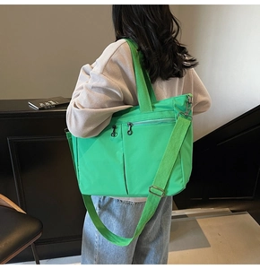 Detail of green tote bag featuring front zipper pockets and adjustable wide shoulder strap