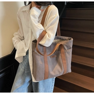 Détail d'un grand sac cabas en toile gris foncé avec anses marron porté à l'épaule, mode