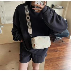 Detail view of a cream canvas crossbody bag with text print on a waffle fabric outfit