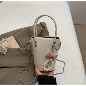 Detail der cremefarbenen Beuteltasche mit Perlenanhänger, rosa Schleife und Kette