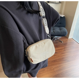 Detail shot of beige canvas camera bag with New Dreams embroidery and wide logo strap