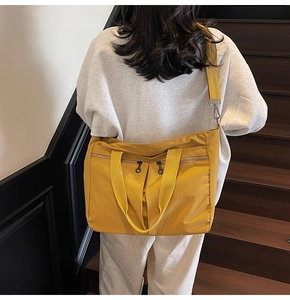 Large yellow nylon tote bag with multiple pockets worn by a model on stairs