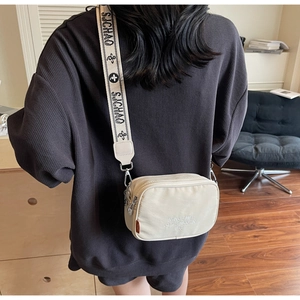 Detail of canvas crossbody camera bag featuring a wide jacquard strap and minimalist design