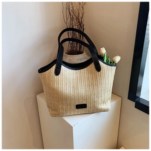 Close-up of woven straw tote bag with black leather handles on a white minimalist pedestal