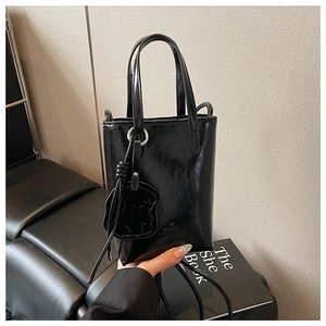 Detail of black glossy leather mini crossbody bag with a cute bear charm accessory