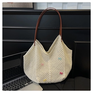 Detail of crochet tote bag with colorful bows and brown leather straps on a dark desk