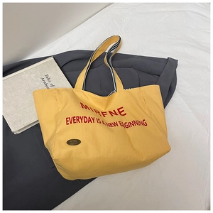 Detail of yellow canvas tote bag with red typography on a soft white fabric background