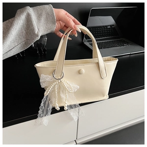 Dettaglio di una borsa a secchiello bianco crema con fiocco in pizzo e perla