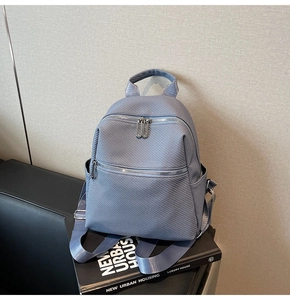 Detail of light blue backpack with quilted texture and silver zipper pockets on urban book