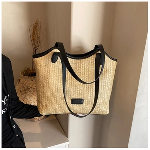 Close-up of beige straw tote bag with black faux leather trim and FASHION logo detail