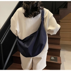 Rear view of a model wearing a large navy blue nylon crescent bag on a wooden staircase