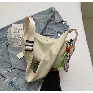 Detail of off-white crescent crossbody bag with adjustable strap and decorative pendant