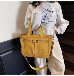 Model wearing a mustard yellow nylon tote bag with double front zippers on stairs